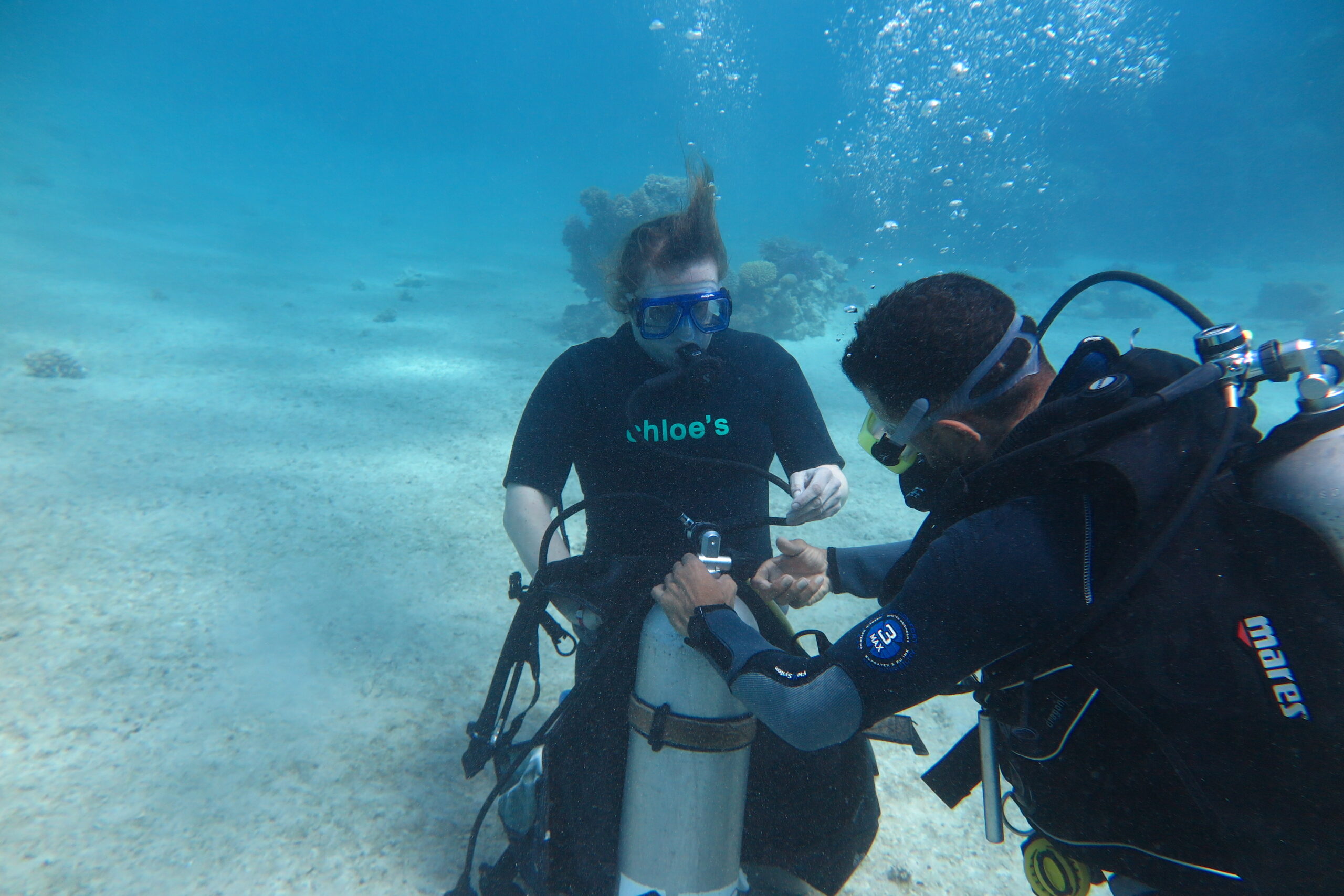 A photo of an instructor from chloes diving center in hurghada helping an open water student to wear the bcd underwater