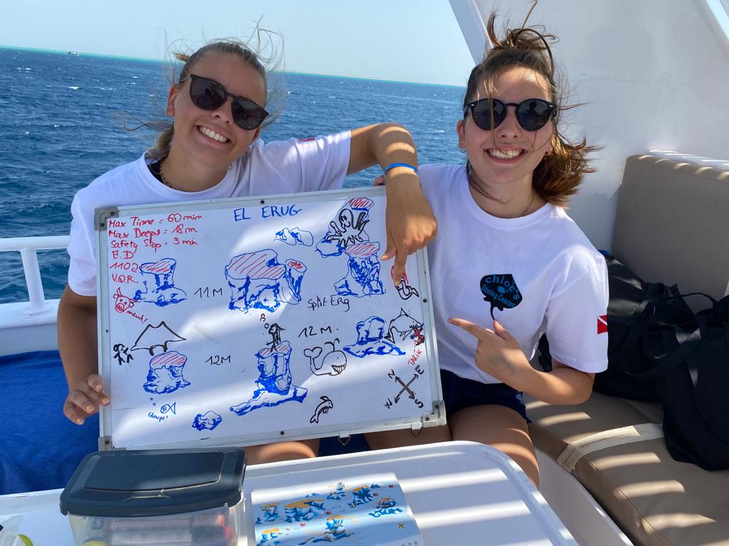 Two beatufil divers with a drawn map on the board of the dive site they're going to dive in with chloes diving center