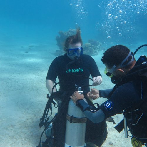 Une photo d'un instructeur du centre de plongée de Chloe à Hurghada aidant un étudiant en eau libre à enfiler son stab sous l'eau.